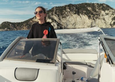 A female traveller taking the wheel of the boat with Marathonisi "Turtle island" as a backdrop.