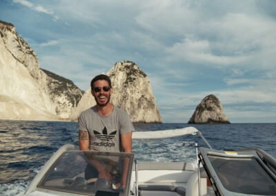 Smiling greek captain behind the wheel of the speedboat with Marathonisi "Turtle island" as a backdrop.