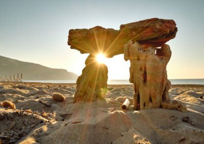 a sunset over the sea and a small rock structure on the beach in front of it