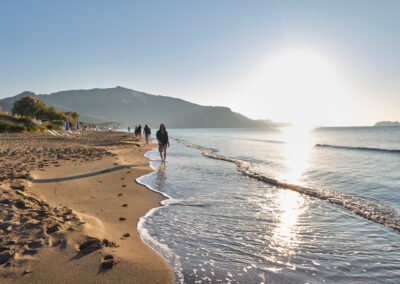 a group of people walking across a beach next to the ocean at sunset times in Zakynthos Kalamaki Beach