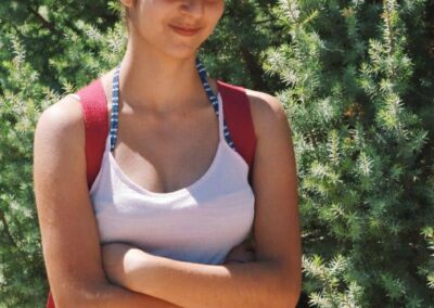 a pretty young lady standing in front of green trees in shorts and a red hat