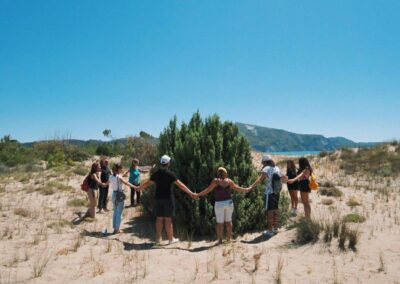 a group of people stand around a tree on a beach with a bluesky background, in Zakynthos island's Sand dunes ecosystem!