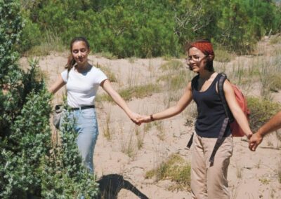 three people standing in front of tall, green bushes and some trees while two hold hands