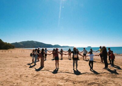 a group of people hold hands on a beach with people walking along the beach in front of them