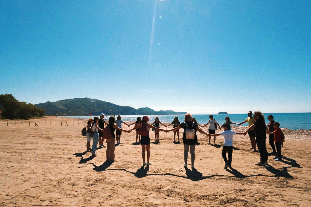 a group of people hold hands on a beach with people walking along the beach in front of them