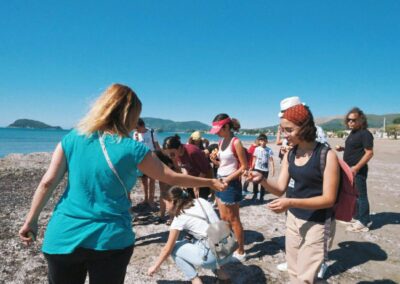 two women shaking hands on the beach while others look on in amazement at the photographer